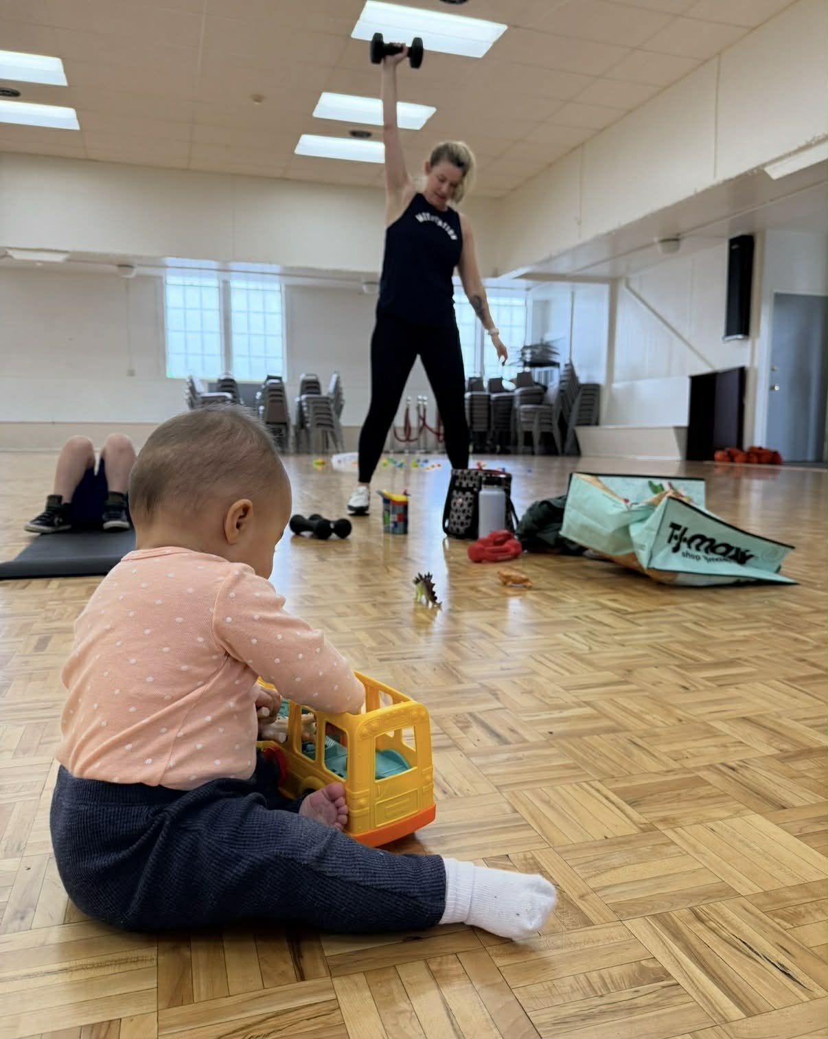 Baby playing with toys while mom works out in the background