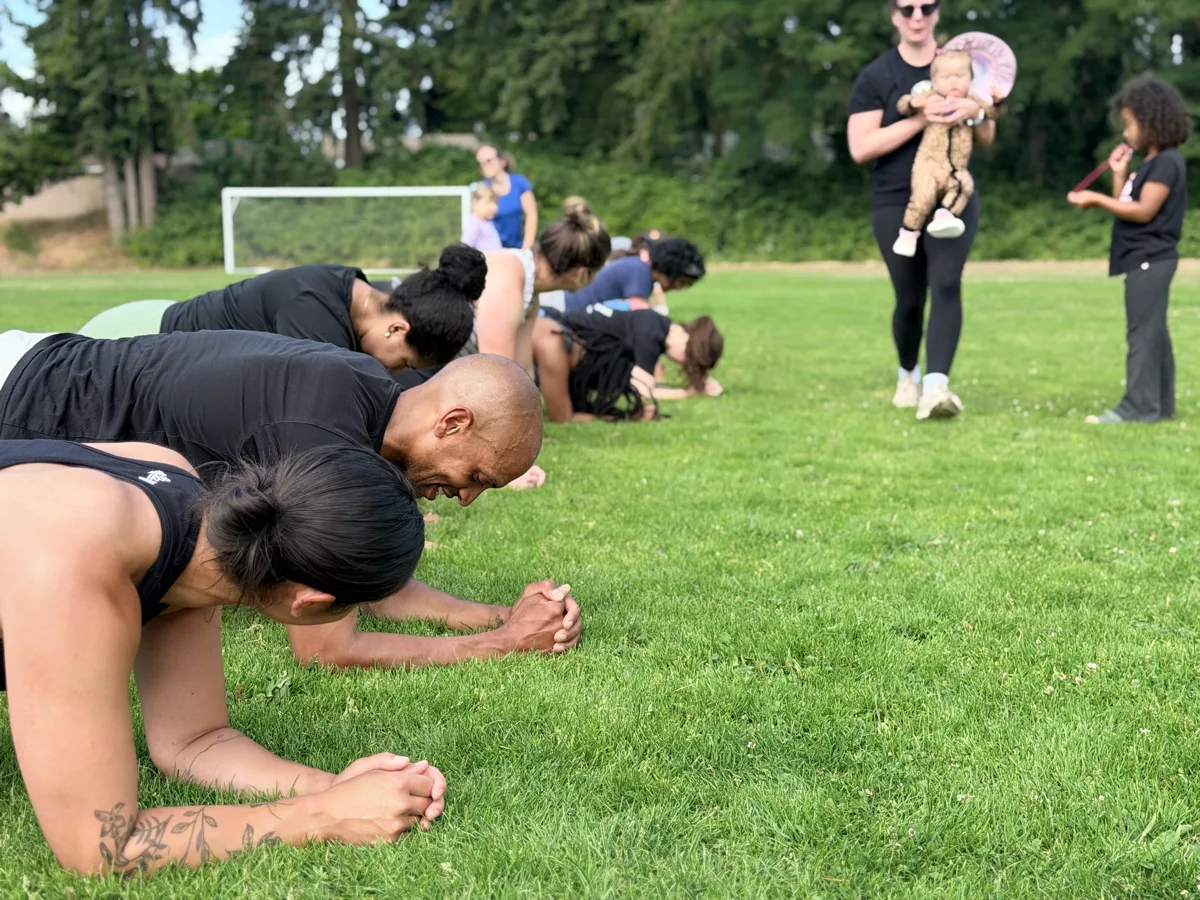 Class members holding a plank line outdoors with kids nearby
